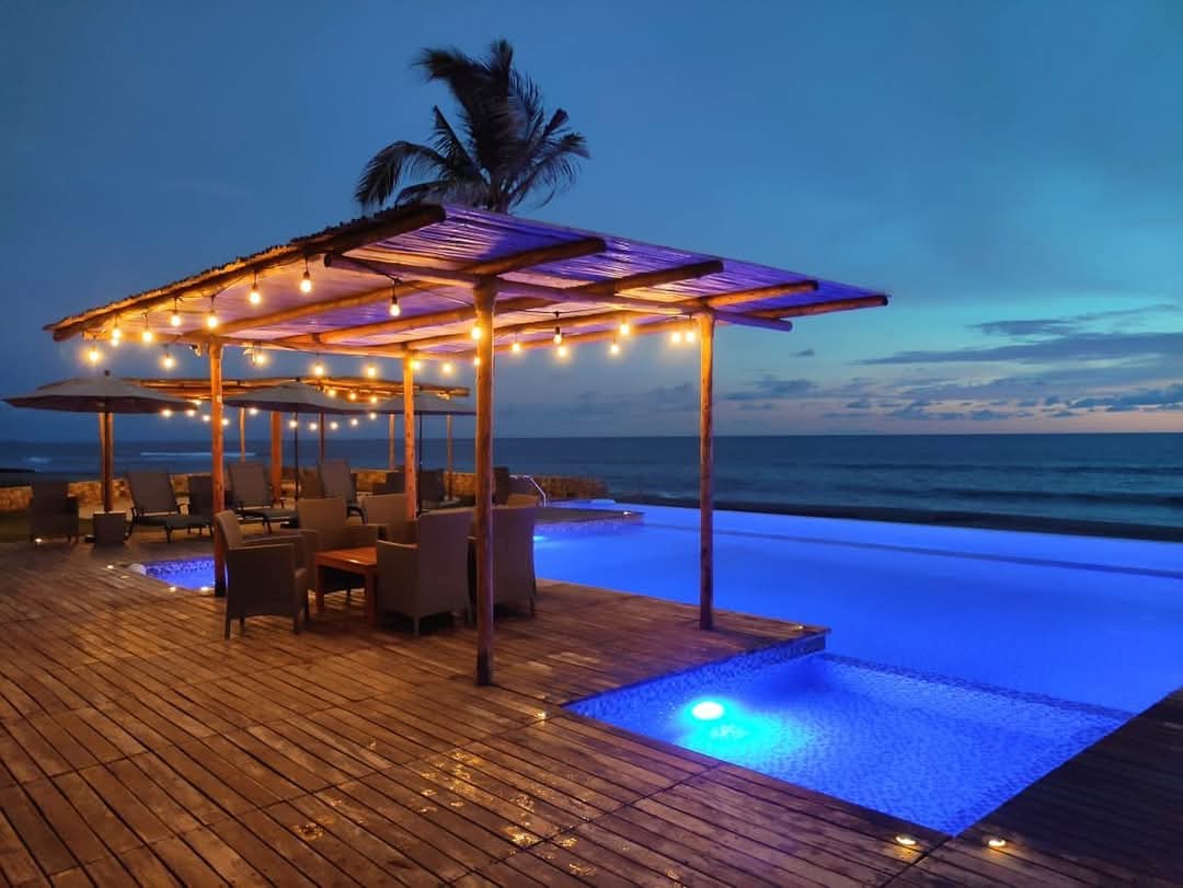 Alberca infinita al anochecer, con pérgola de luces y el mar al fondo