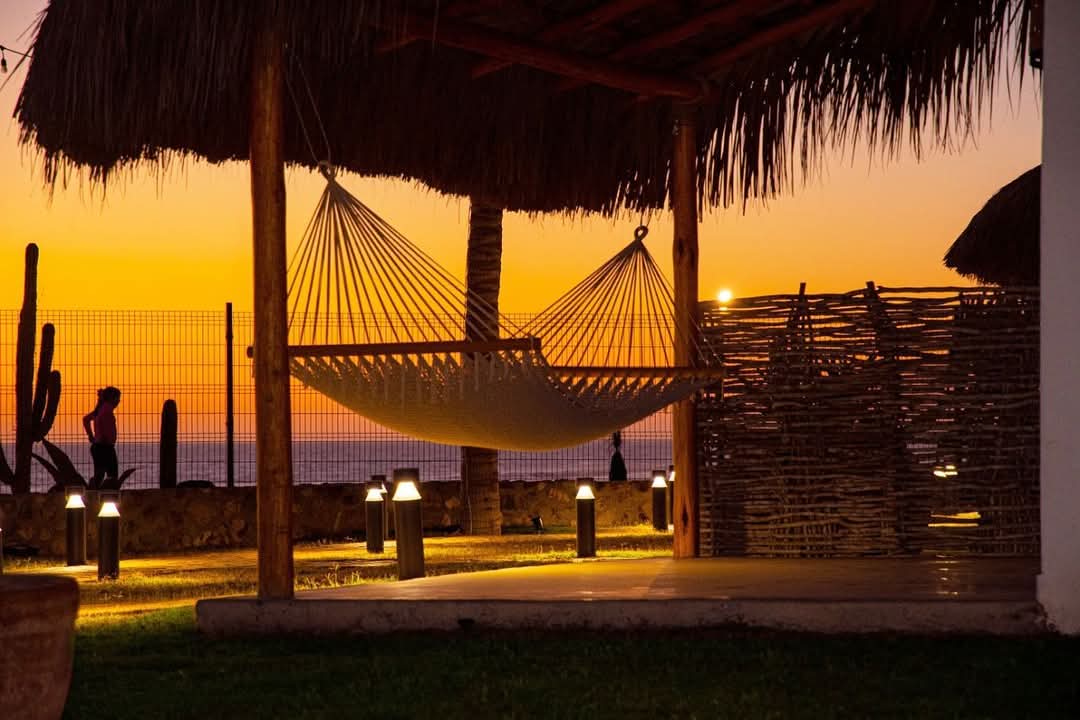 Hamaca bajo palapa recortada contra el sol que se mete en el mar