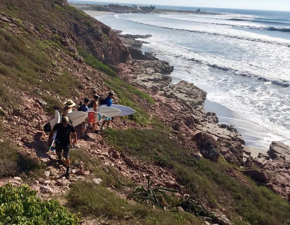 Surfistas bajando por la punta rocosa mientras la izquierda se desdobla a lo largo de la orilla