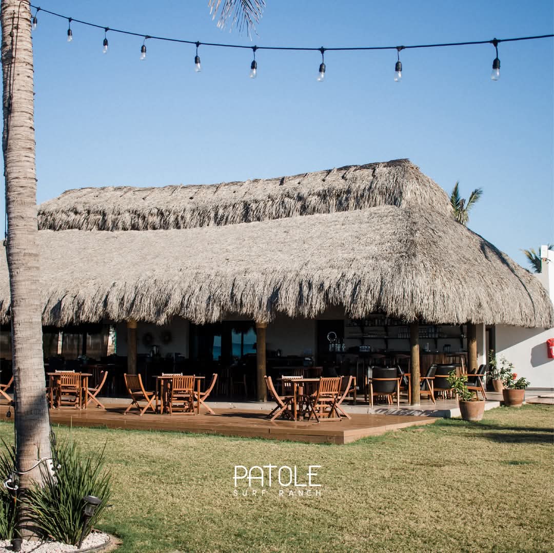 Restaurante bajo palapa de zacate con mesas de madera en la terraza